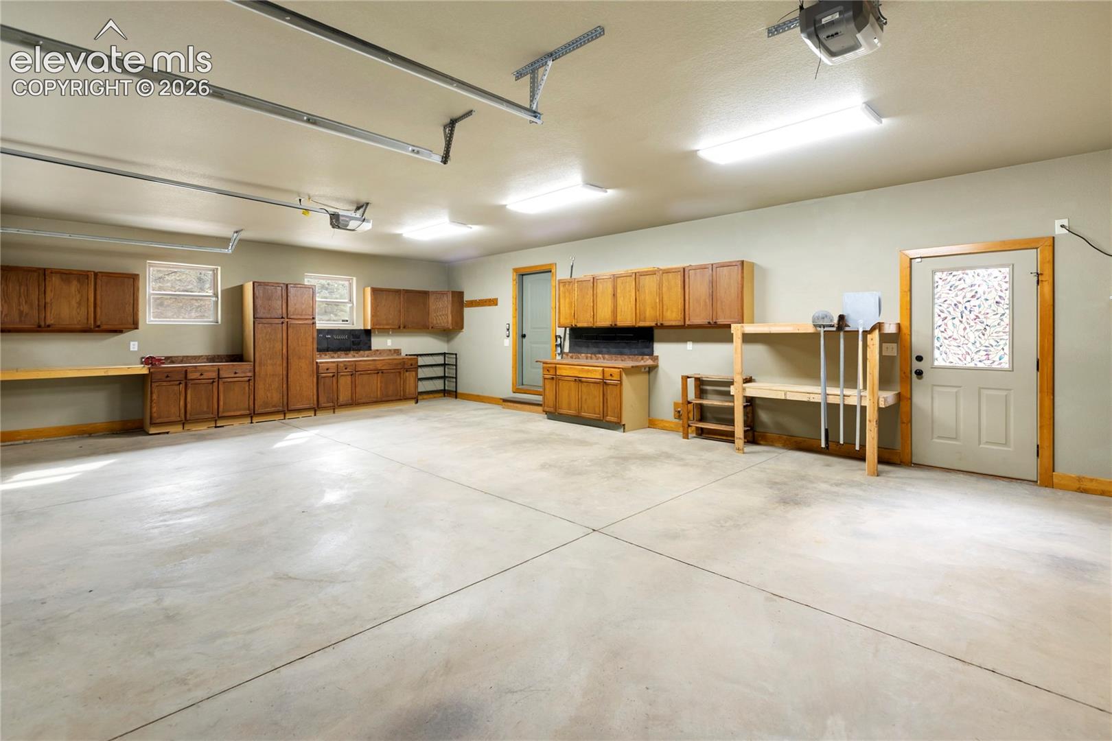 Multi-car garage featuring extensive wood-finish cabinetry, concrete flooring, dual overhead door openers, and a side-entry door with inset decorative glass