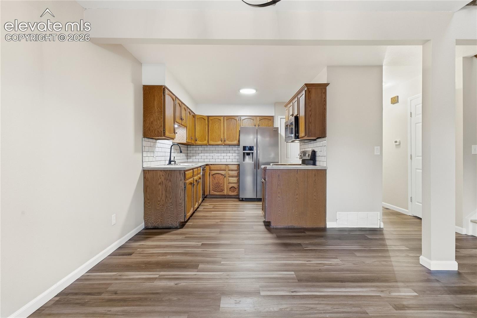 Kitchen featuring wood-finish cabinetry, white subway tile backsplash, stainless steel appliances, and a matte black faucet