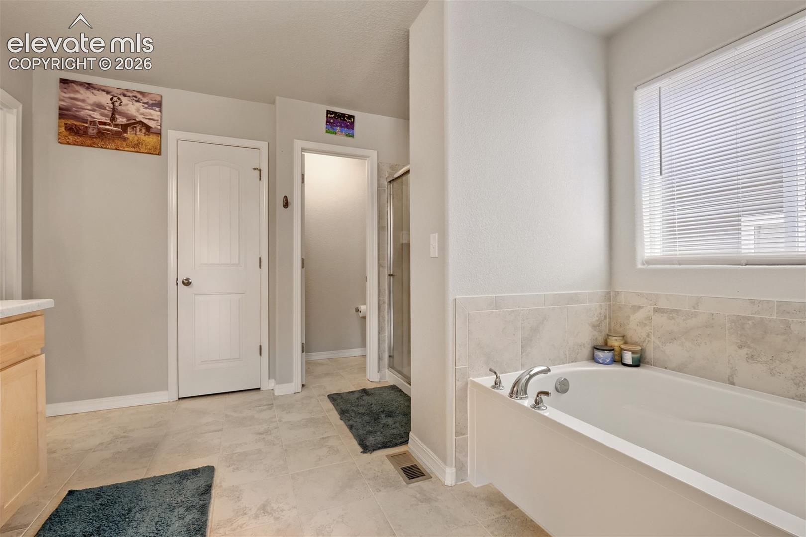 Soaking tub with chrome fixtures, surrounded by light-toned tile wainscoting