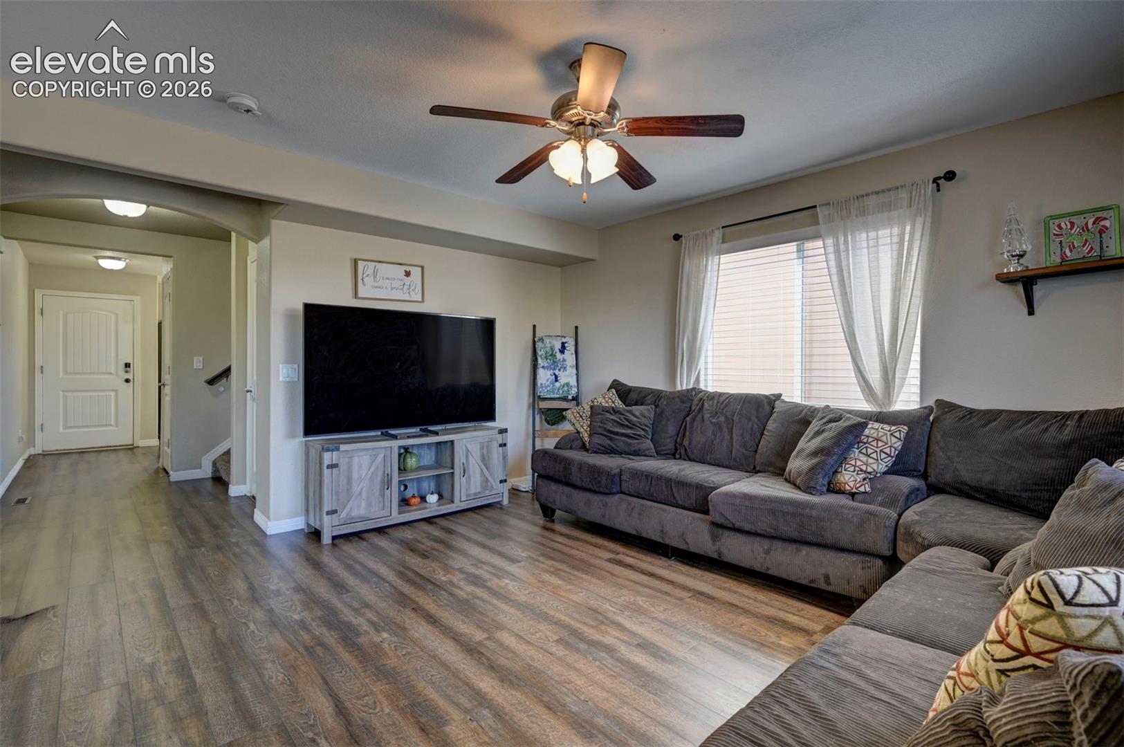 Open living area featuring wood-finish flooring, an arched entryway, and a ceiling fan with integrated lighting