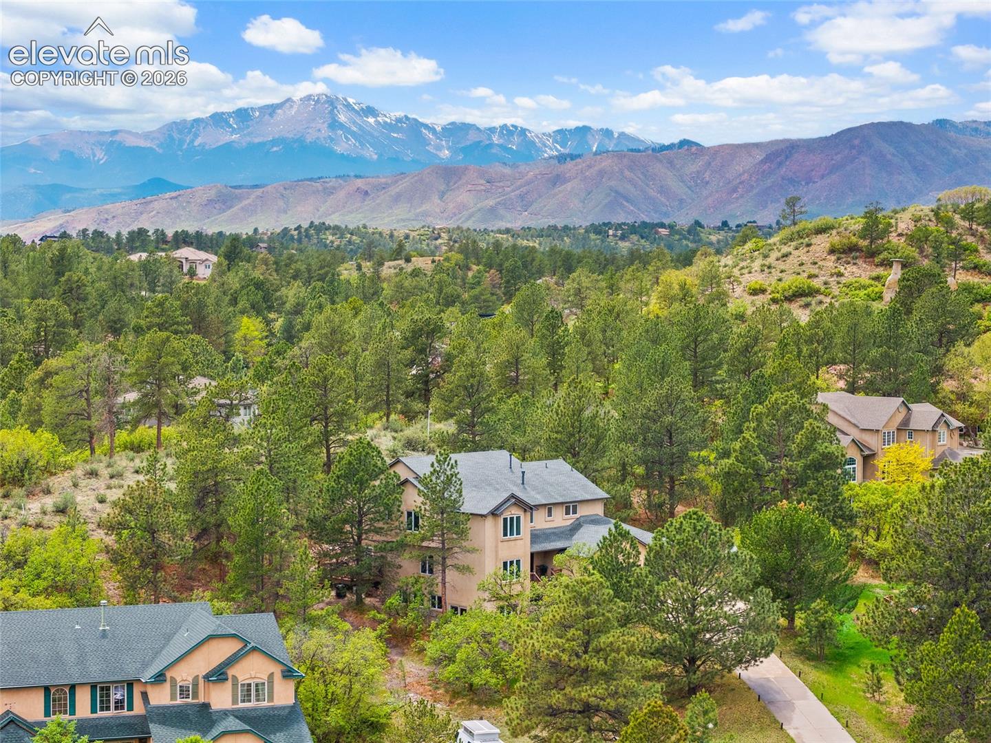 Multi-level stucco exterior with a composite shingle roof, surrounded by mature pine trees and mountain topography