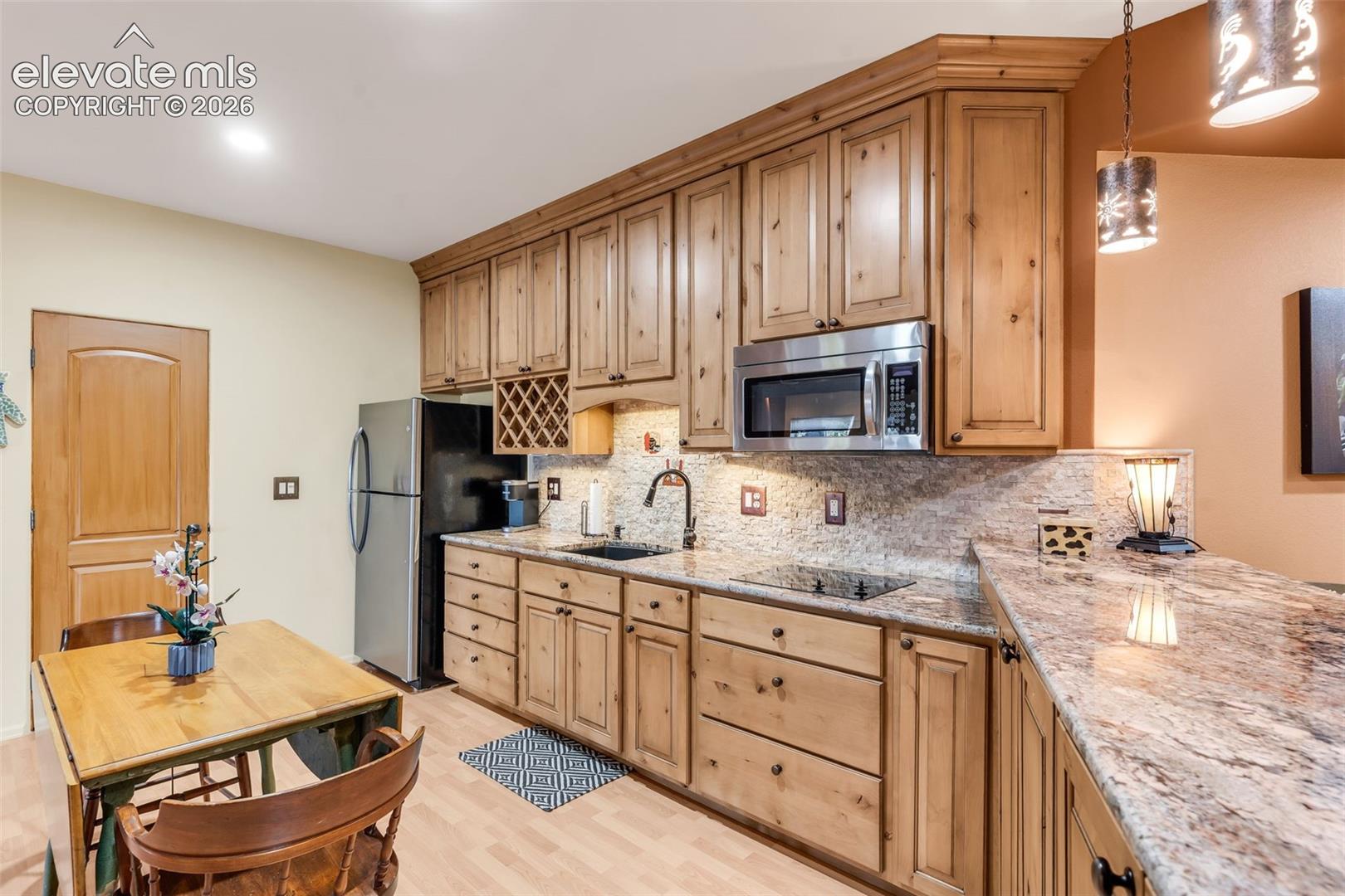 Kitchen featuring knotty wood cabinetry, natural stone countertops, a built-in wine rack, stone tile backsplash, and a breakfast bar