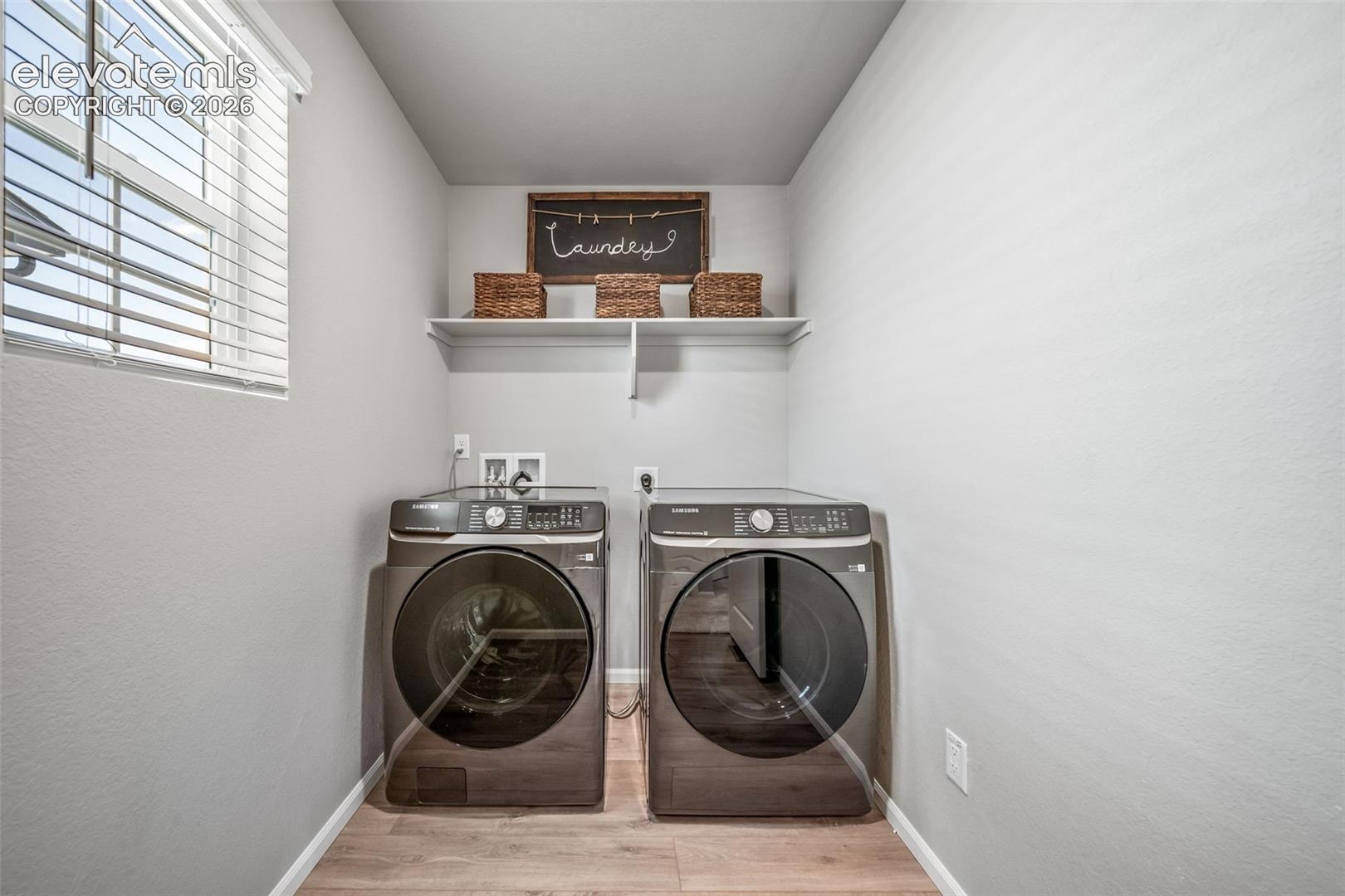 Dedicated laundry room featuring side-by-side front-load washers and dryers with stainless steel finishes, wood-finish flooring, and ample shelving for storage and organization
*photos of a model home*