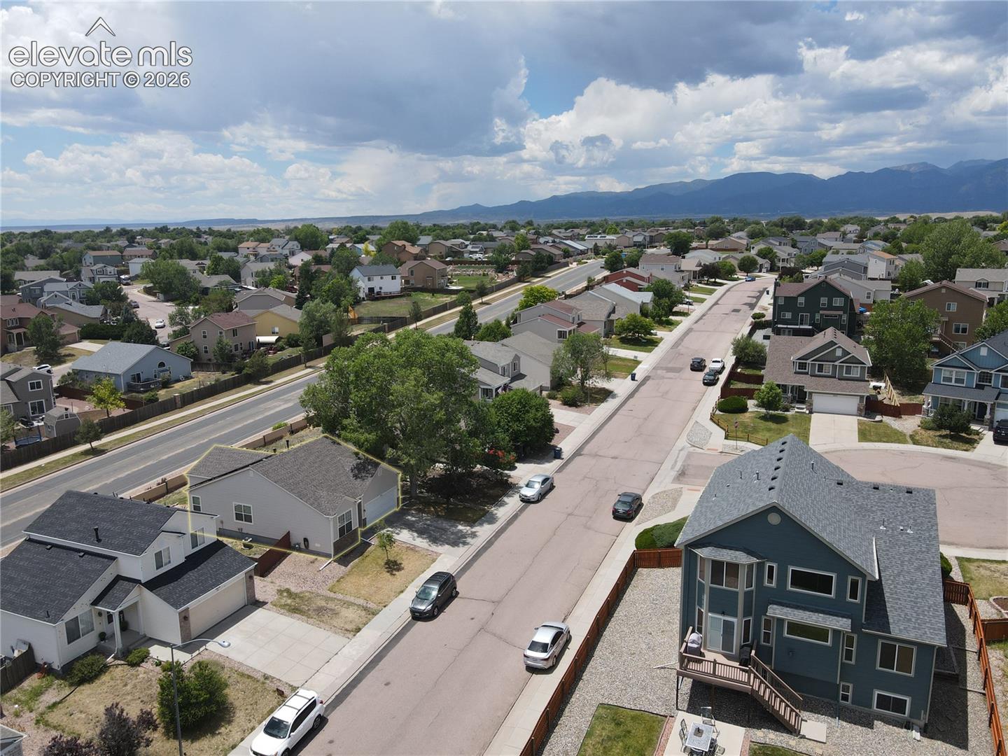Suburban street with residential properties featuring various architectural styles, concrete sidewalks, and mature trees