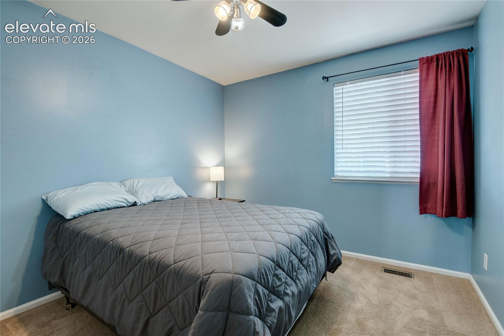 Carpeted room featuring a ceiling fan with integrated lighting, a window with horizontal blinds, and light blue wall finishes