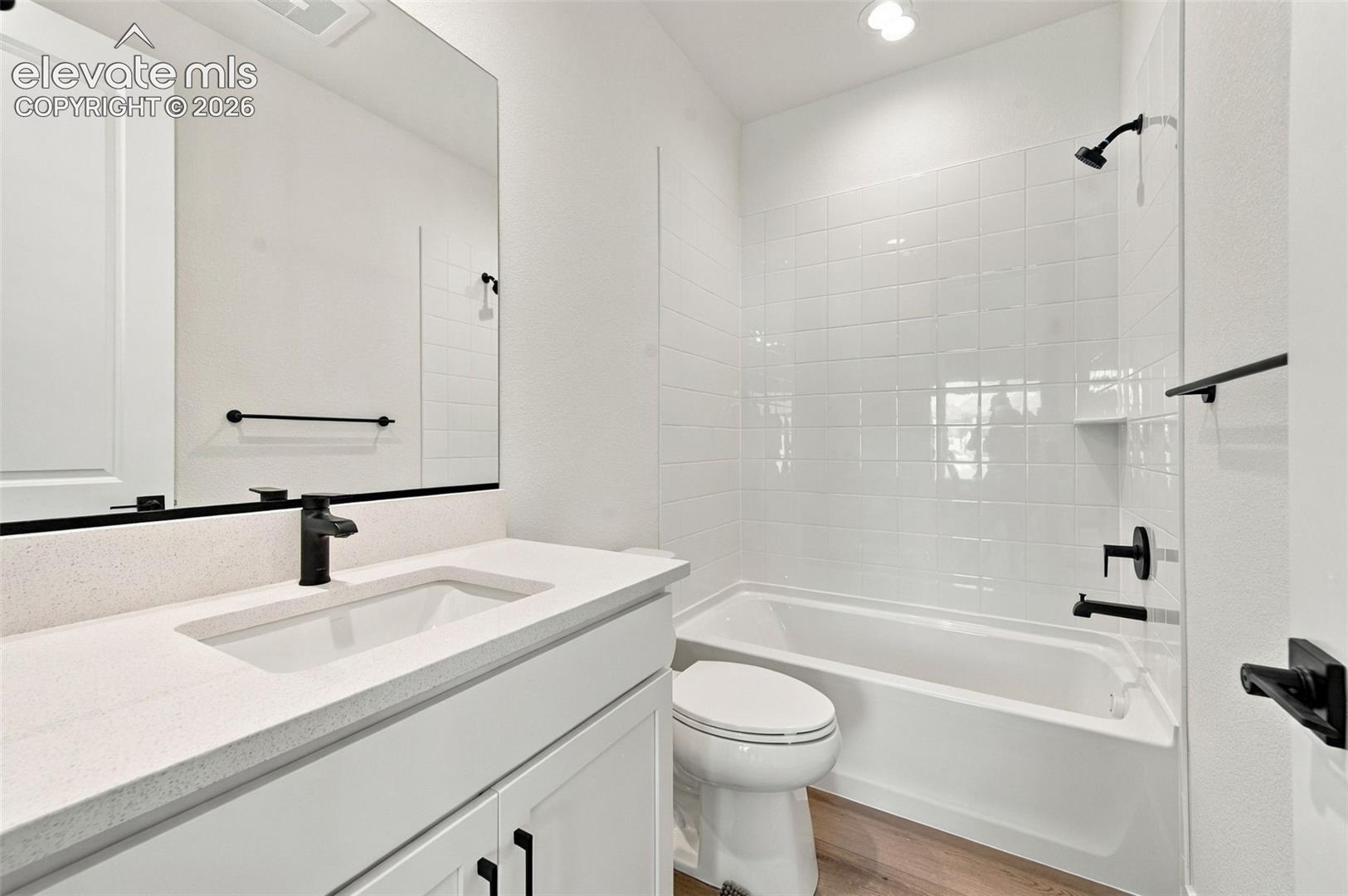 Bathroom featuring a stone-surface vanity with a rectangular sink, matte black fixtures, a wall-to-wall mirror, and a tile-surround tub with shower