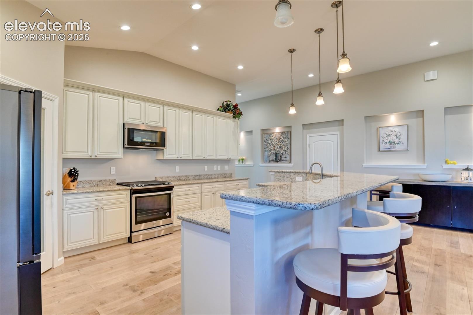 Kitchen featuring light-finish cabinetry, granite countertops, stainless steel appliances, and wood-finish flooring.