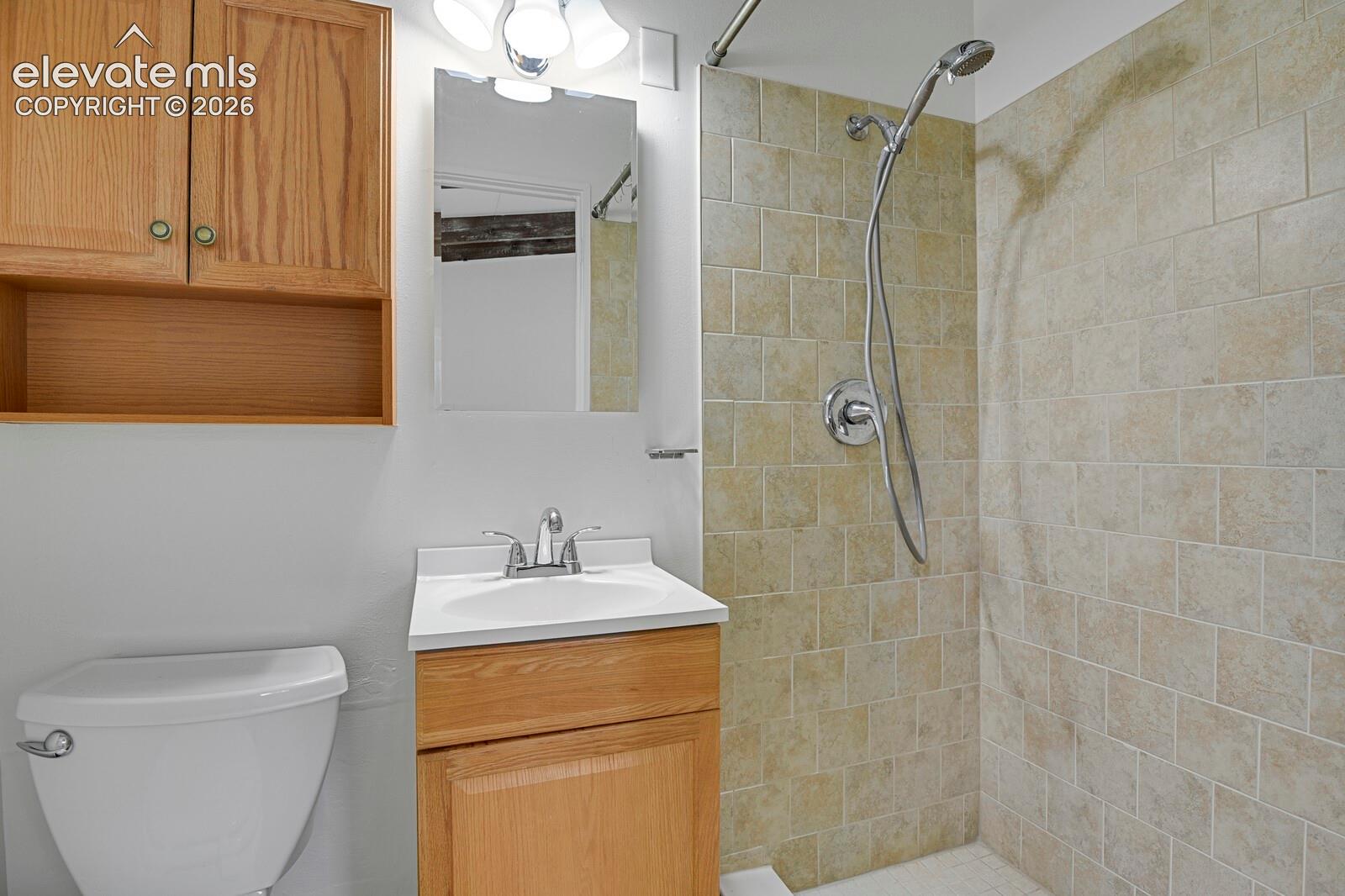 Bathroom featuring a wood-finish vanity with an integrated sink, wall-mounted upper cabinetry, a shower with stone-tile surround, and a handheld shower fixture