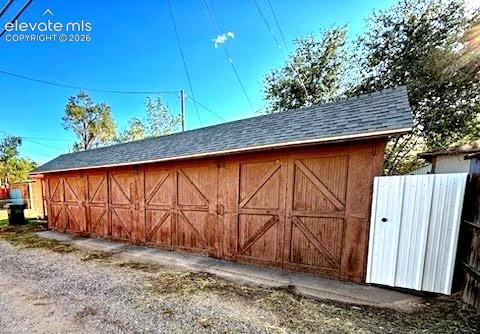 Multi-bay detached garage featuring wood-paneled exterior doors with cross-bracing details and a pitched asphalt shingle roof
