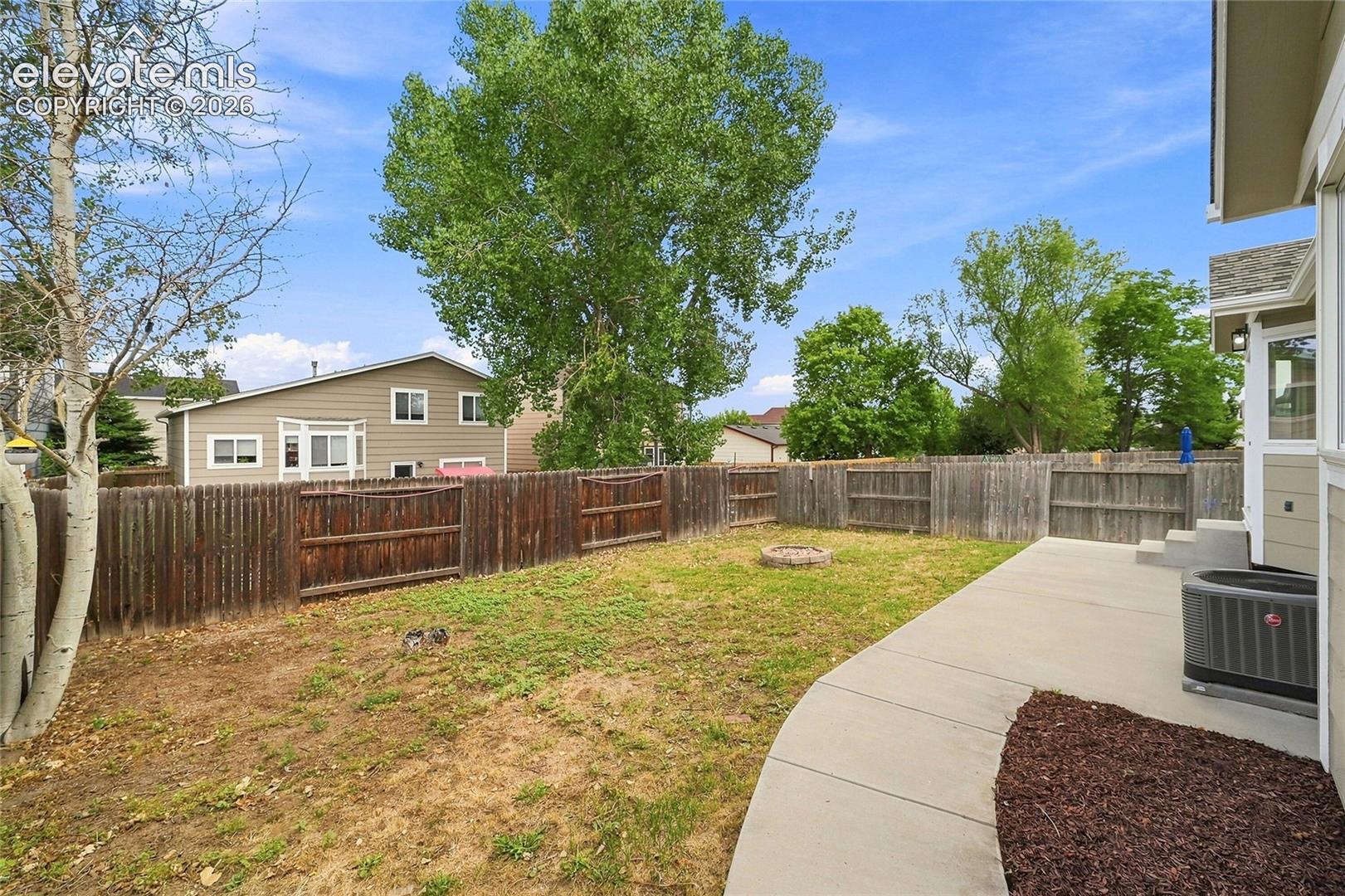 Fenced backyard featuring a concrete patio, a fire pit, and mature trees