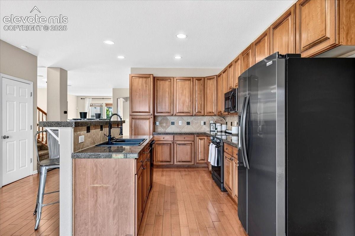 Kitchen featuring wood-finish flooring, wood cabinetry, granite countertops, and black appliances
