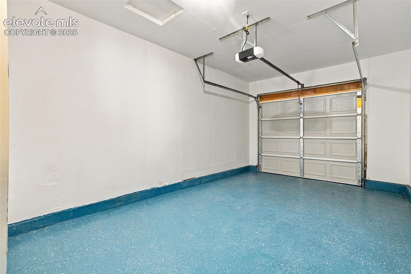 Garage space featuring a painted concrete floor with an epoxy finish, finished walls, an overhead garage door, and a ceiling-mounted automatic door opener