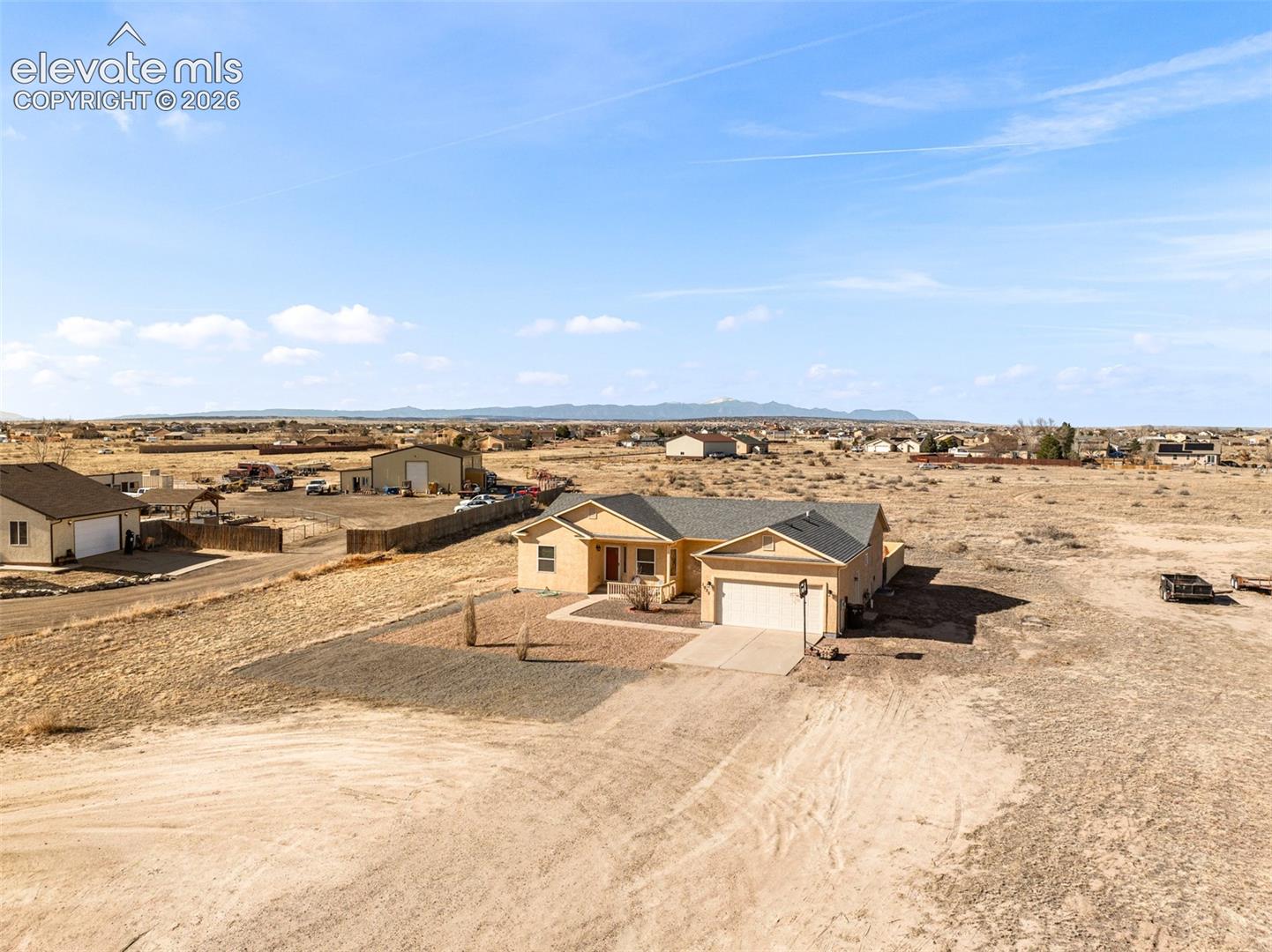 Single-story residence featuring a two-car garage, pitched roof, and an open front yard with a gravel driveway