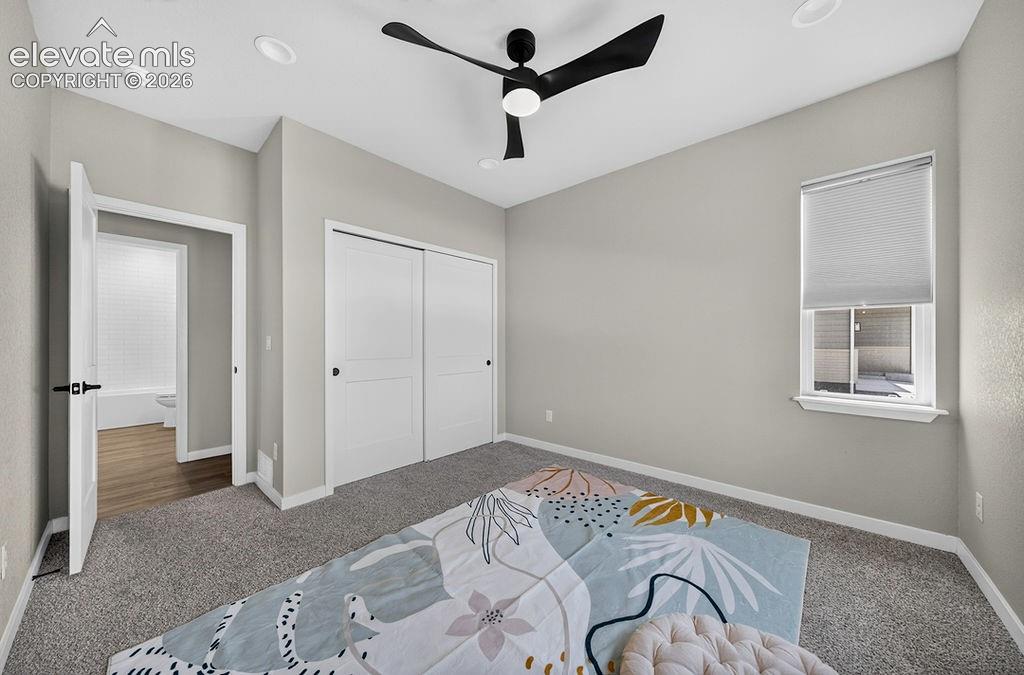 Carpeted room with light grey walls, featuring a modern black ceiling fan with integrated lighting, recessed ceiling lights, and white trim