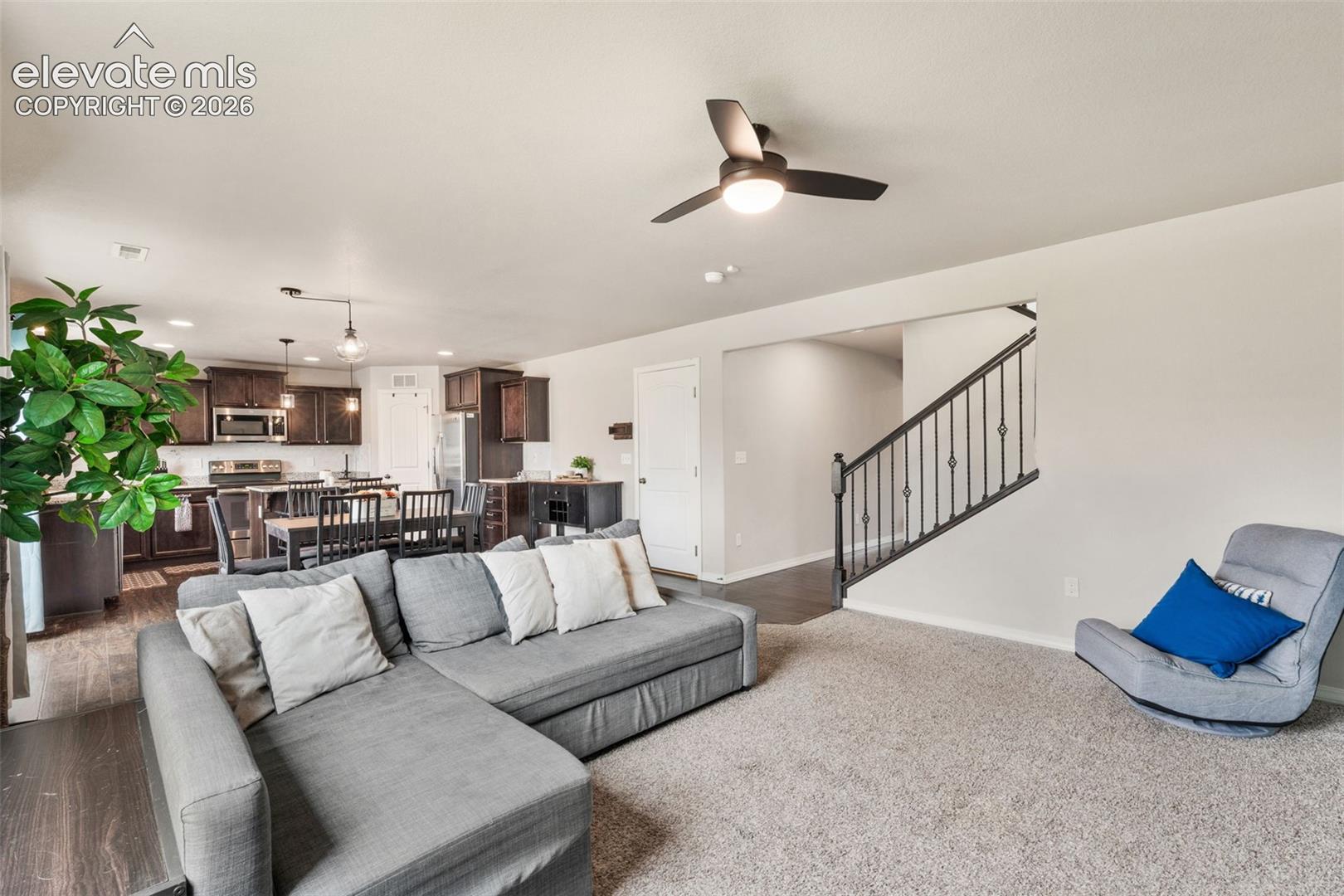 Open-concept living area featuring a ceiling fan, dark wood-finish flooring, and light-toned carpeting