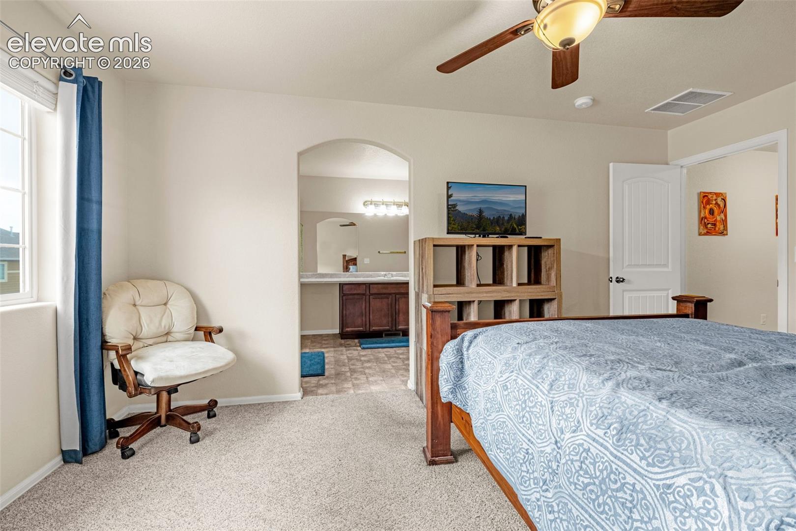 Carpeted bedroom with a ceiling fan, arched doorway, and window with blinds