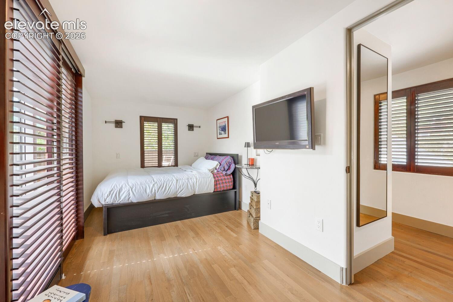 Hardwood flooring, wall-mounted sconce lighting, and wood-toned louvered window treatments