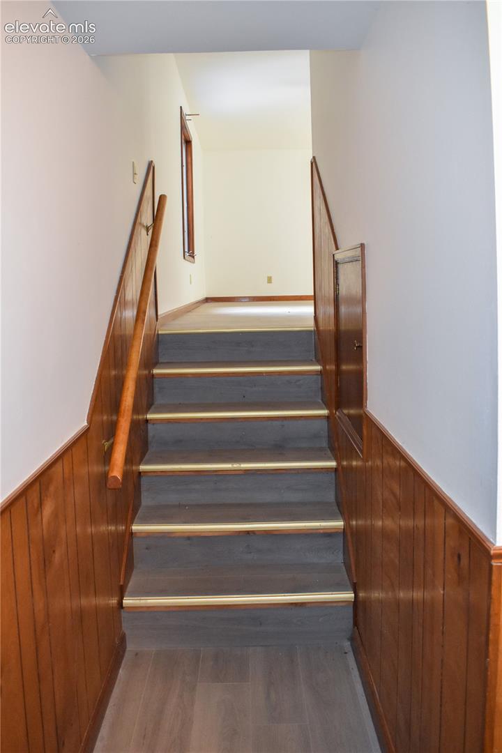 Staircase featuring wood-finish treads with brass accents, wood paneling, and a wood handrail