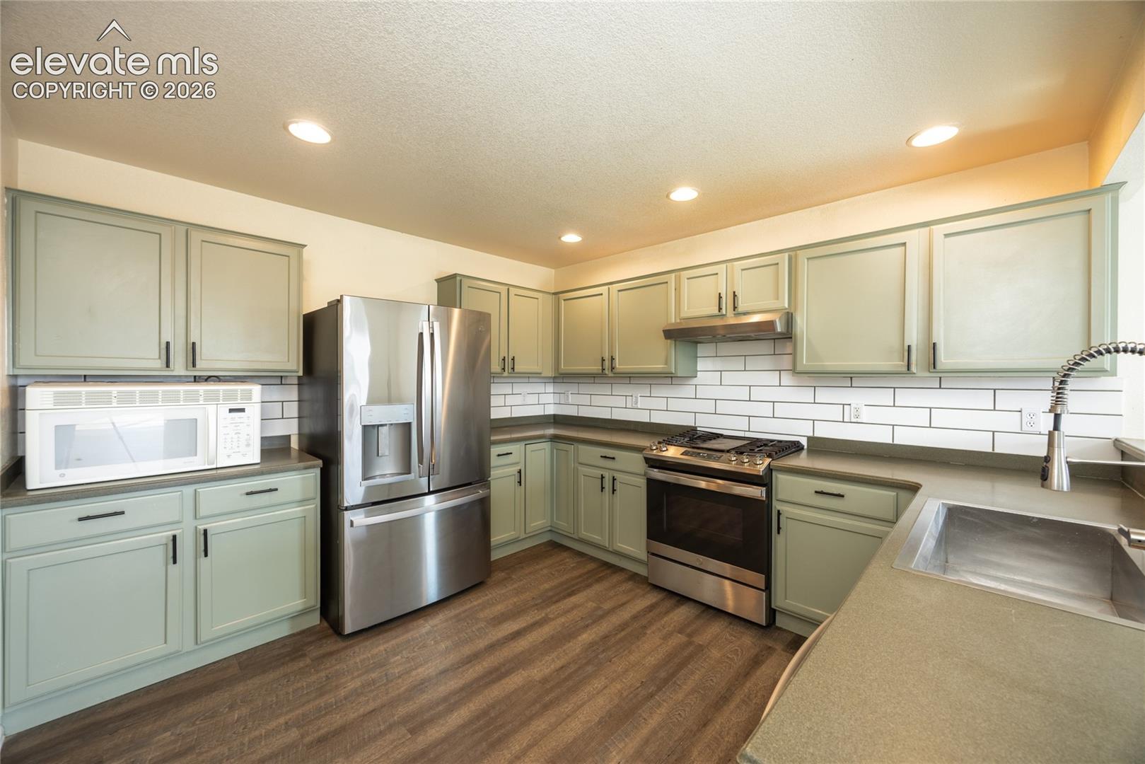 Kitchen featuring light green cabinetry, stainless steel appliances, subway tile backsplash, recessed lighting, and wood-finish flooring