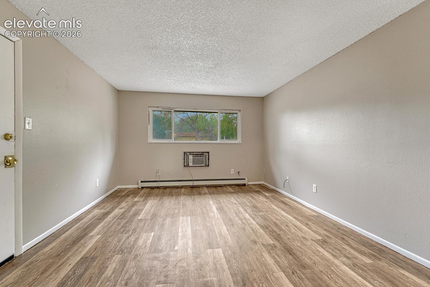 Wood-finish flooring throughout, neutral wall paint, and a window unit air conditioner