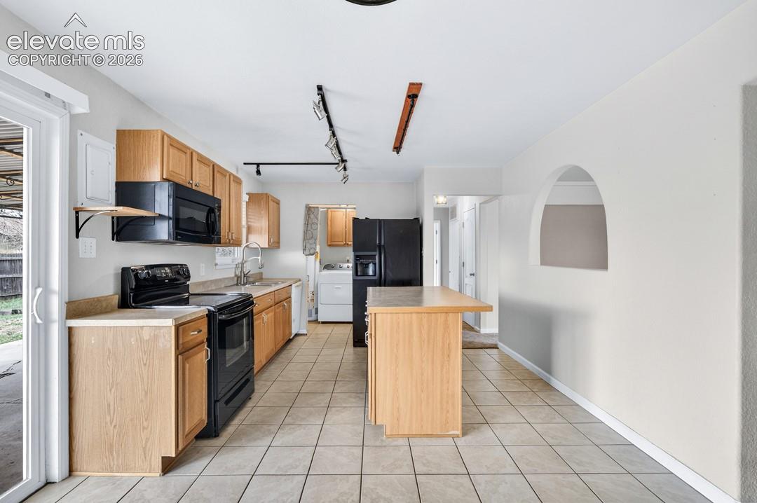Kitchen with wood cabinetry, black appliances, tile flooring, and a center island