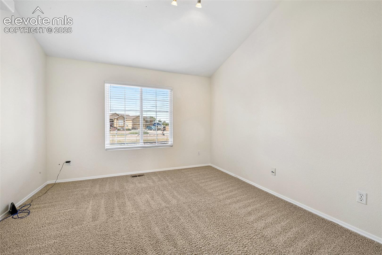 Vaulted ceiling, neutral wall paint, carpeted flooring, and a window with blinds, Could be an office 