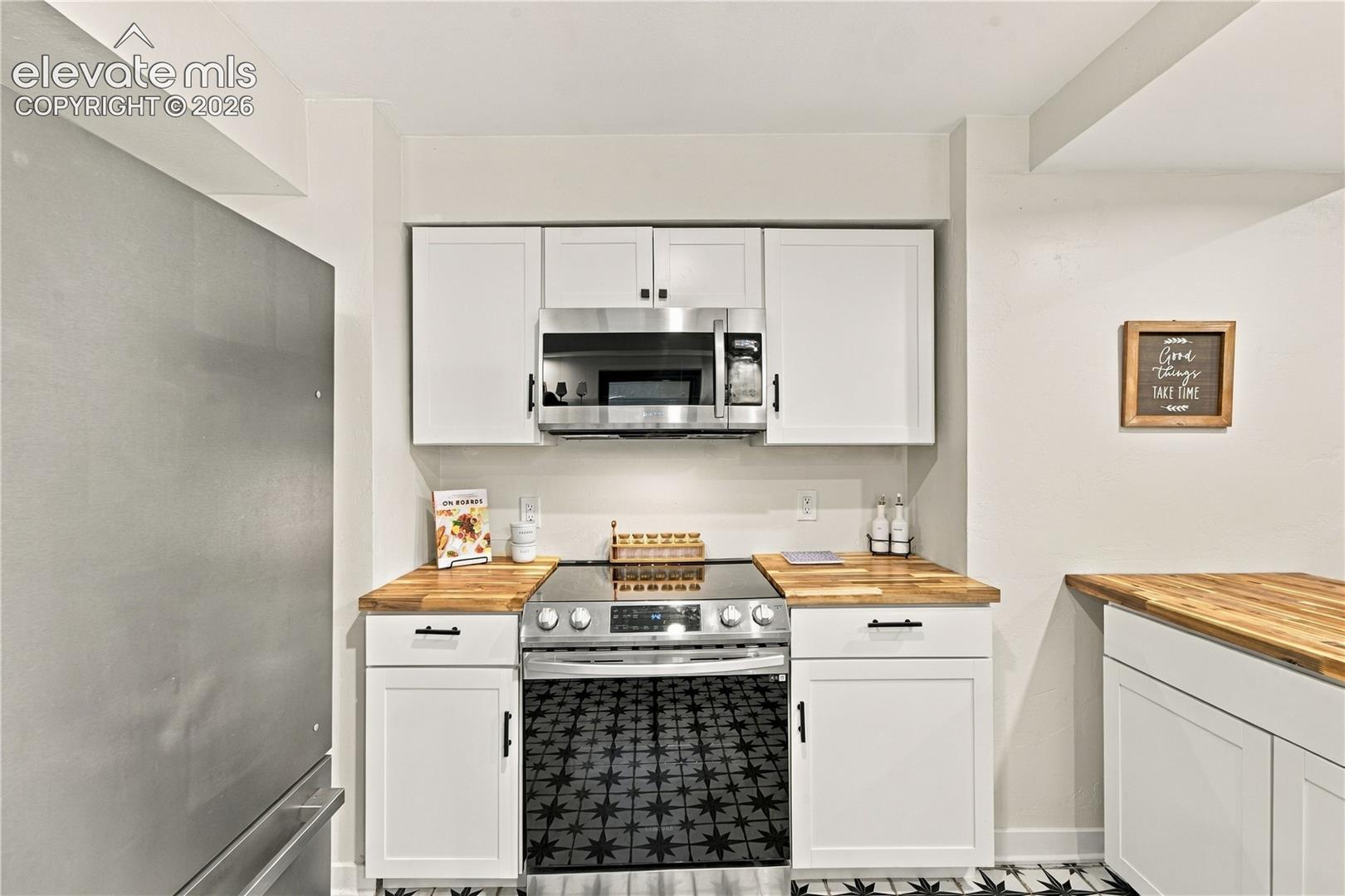 Kitchen featuring white shaker-style cabinetry, wood-finish countertops, stainless steel appliances, and a patterned tile floor