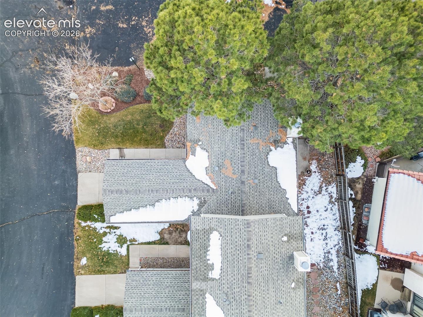 Aerial perspective of property featuring shingle roofing, masonry chimney, mature evergreen trees, and xeriscaped lot