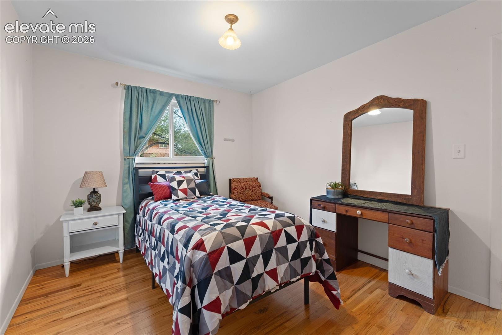 Hardwood flooring, painted white walls, ceiling-mounted light fixture, and window with outdoor scenery