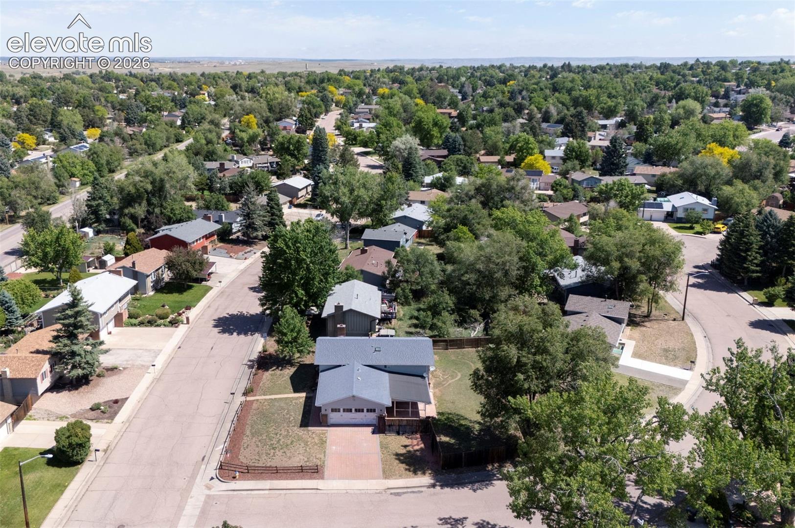 Aerial perspective featuring a multi-level residential exterior with a paved driveway, attached two-car garage, and established tree canopy