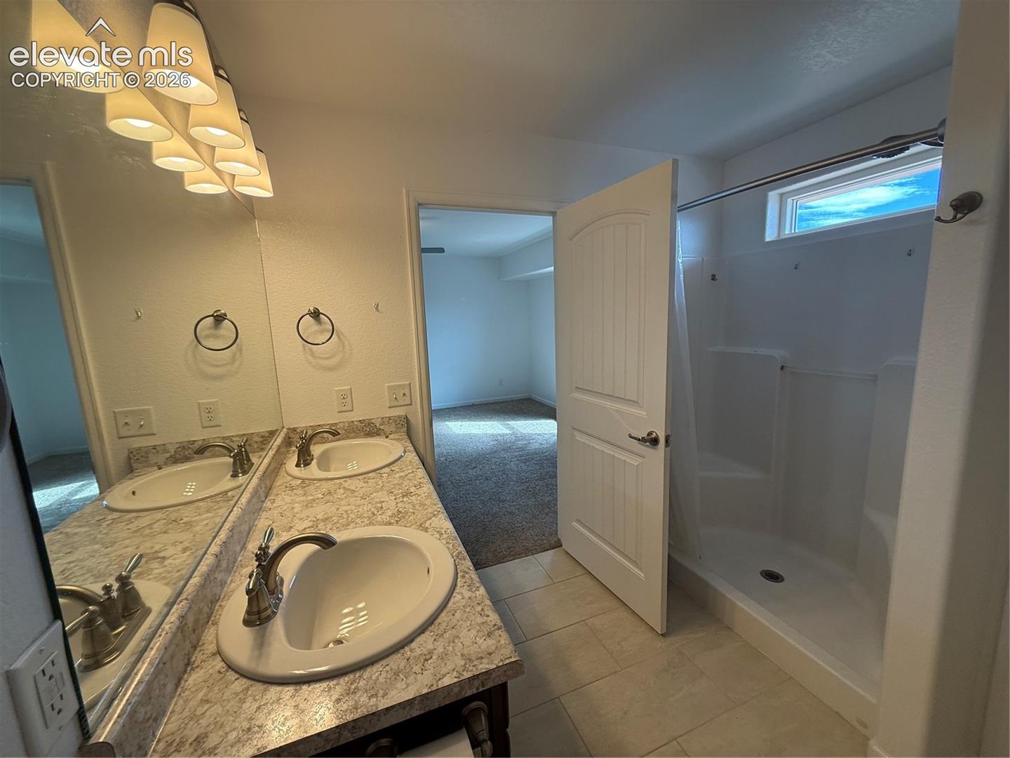 Dual-sink vanity with a stone-finish countertop, under-mount basins, polished metal fixtures, and a glass-enclosed shower surround featuring ceramic tile flooring