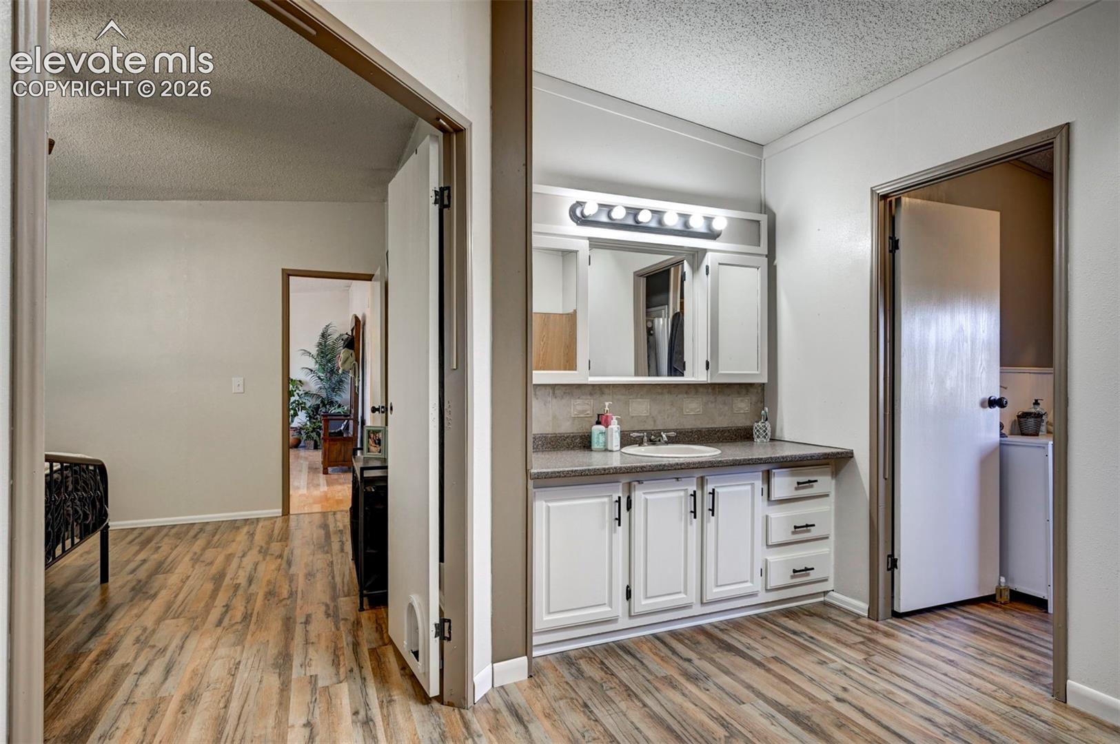 Bathroom with a textured ceiling, light wood-style floors, vanity, and decorative backsplash
