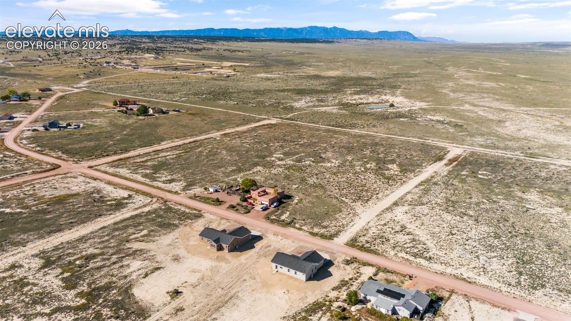 Aerial perspective of a sprawling land parcel featuring extensive open acreage, unpaved road frontage, and a mountain range backdrop