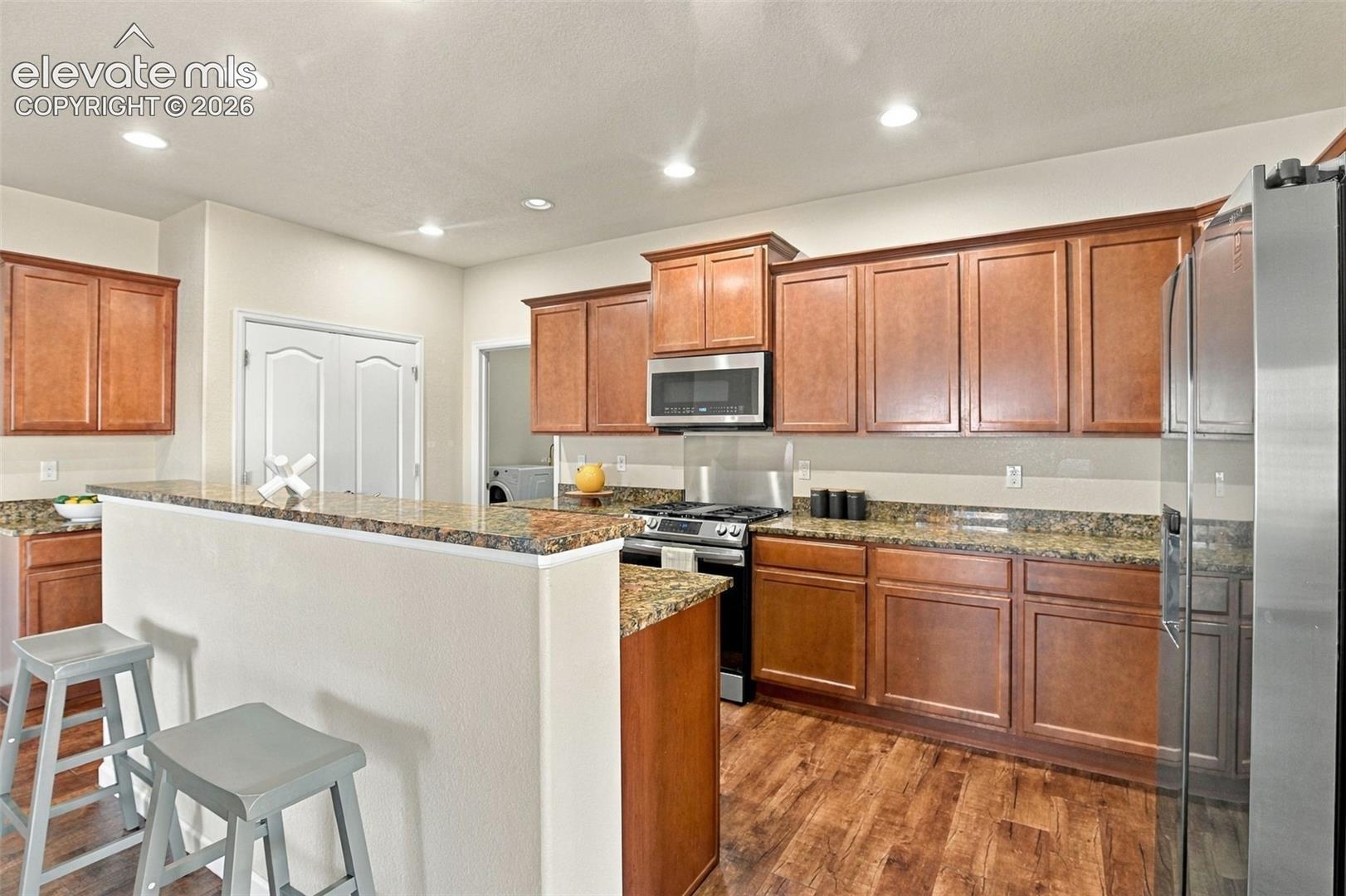Kitchen featuring wood cabinetry, stone countertops, stainless steel appliances, recessed lighting, and wood-finish flooring