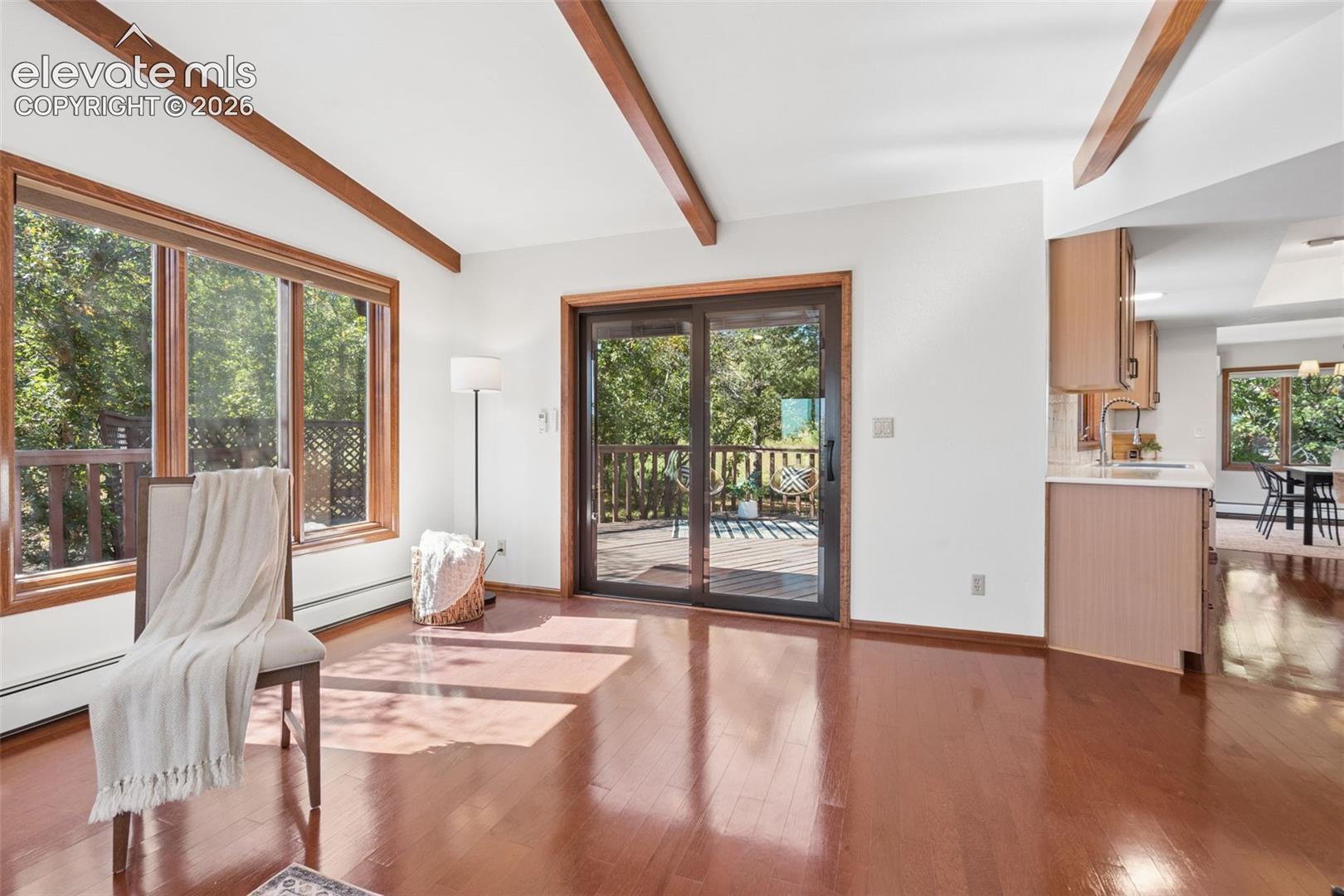 Warm wood-finish flooring, exposed ceiling beams, large picture windows, and a sliding glass door to an outdoor deck
