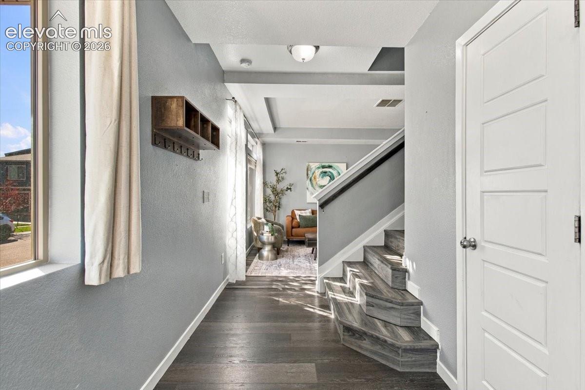 Wood-finish flooring, staircase with dark treads and white risers, contemporary paneled interior door, recessed lighting, and a built-in wall shelf with hooks