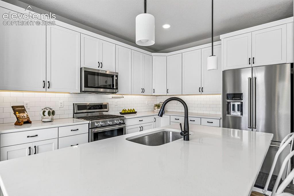 Modern kitchen featuring an expansive island with an undermount sink and matte black faucet, white shaker-style cabinetry, stainless steel appliances, and subway tile backsplash