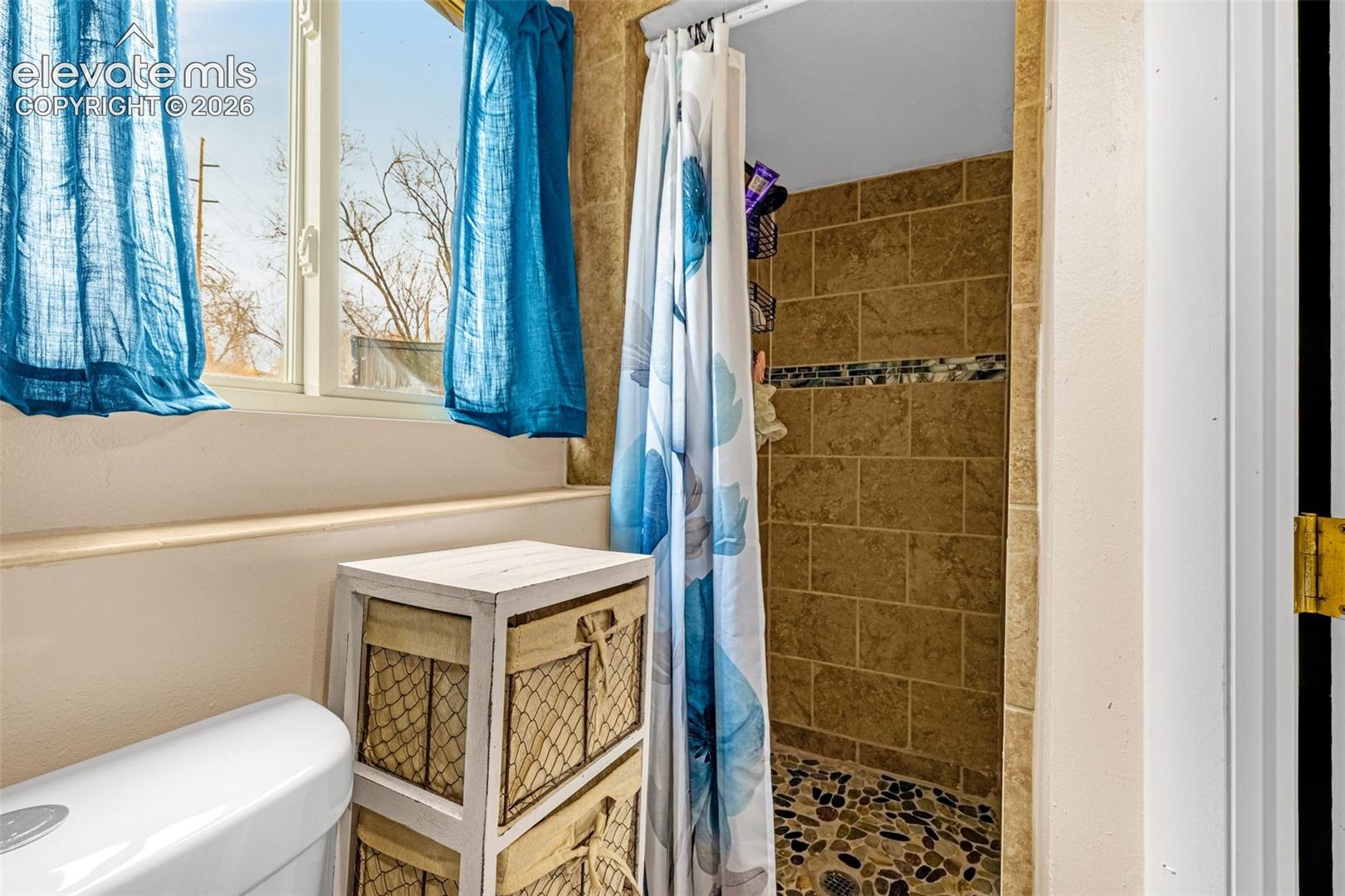 Bathroom featuring a shower stall with stone-tile surround, river-rock flooring, and a glass-tile inlay accent