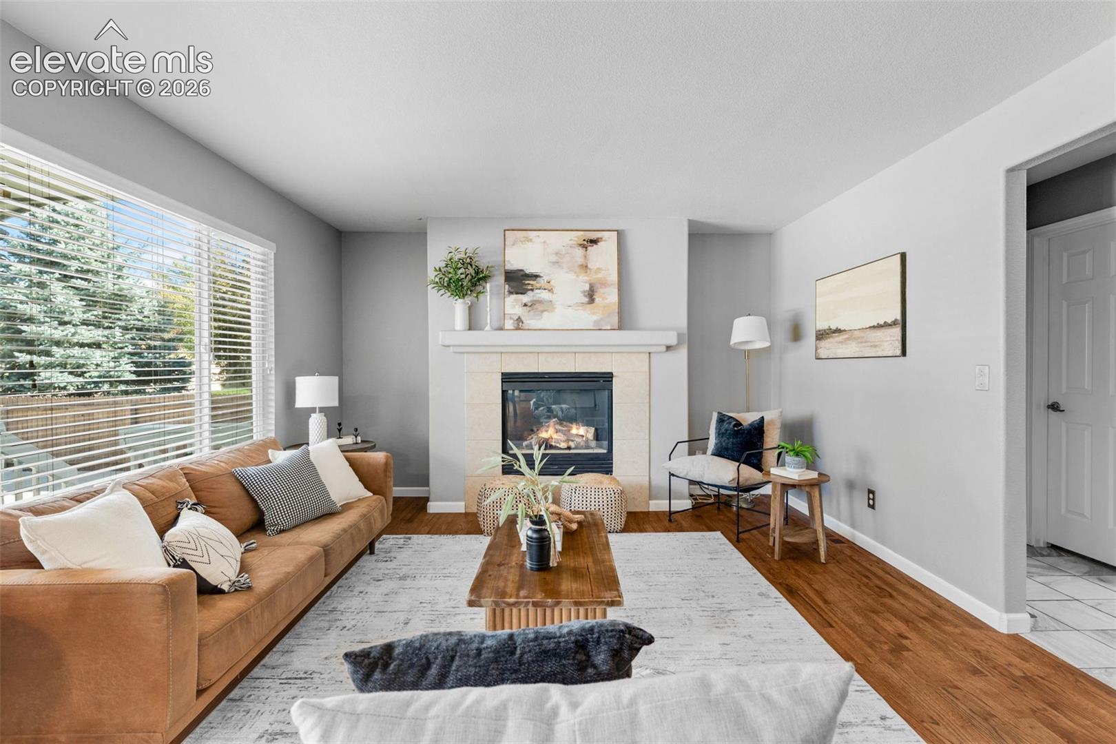 Living room featuring wood-finish flooring, a fireplace with a neutral-toned surround, a prominent mantel, and oversized windows