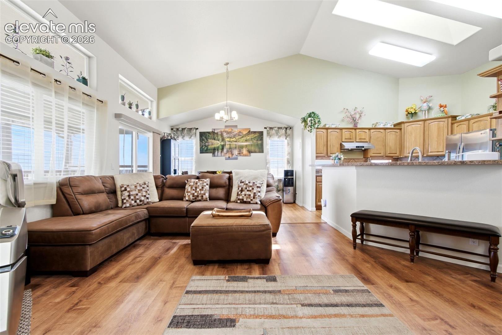 Open-concept living area featuring warm laminate wood-finish flooring, vaulted ceilings with skylights, and stainless steel kitchen appliances