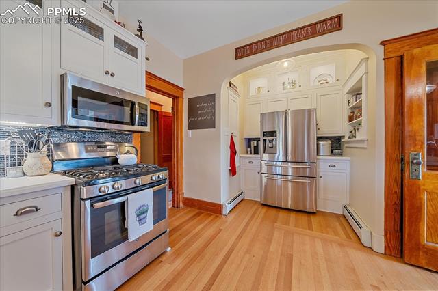 Kitchen with appliances with stainless steel finishes, arched walkways, light wood finished floors, decorative backsplash, and light countertops