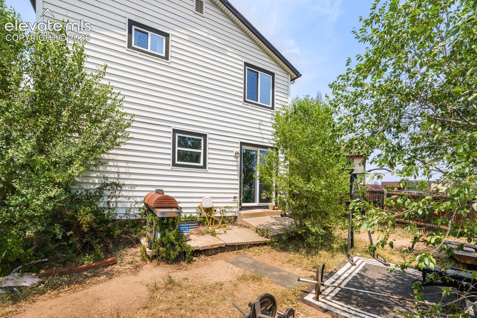 White horizontal siding exterior with black trim windows, a concrete patio, and a sliding glass door