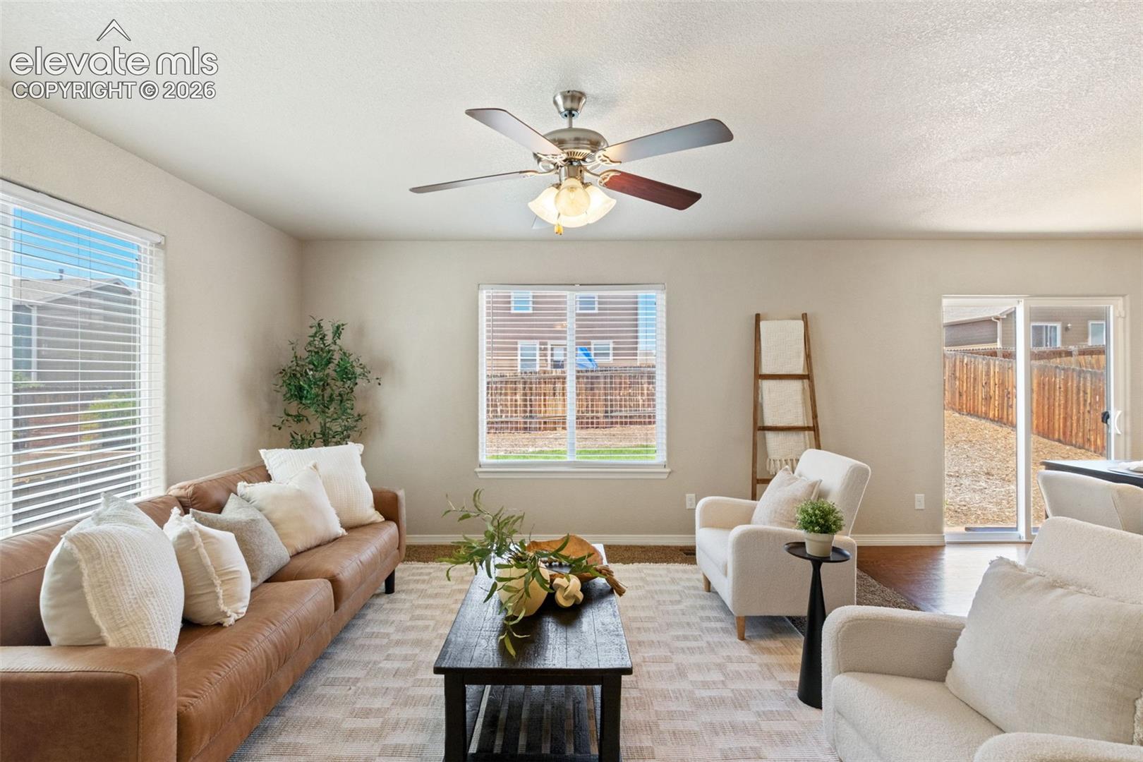 Living area featuring neutral wall tones, multiple windows with blinds, a ceiling fan with integrated lighting, wood-finish flooring, and a sliding glass door to the exterior