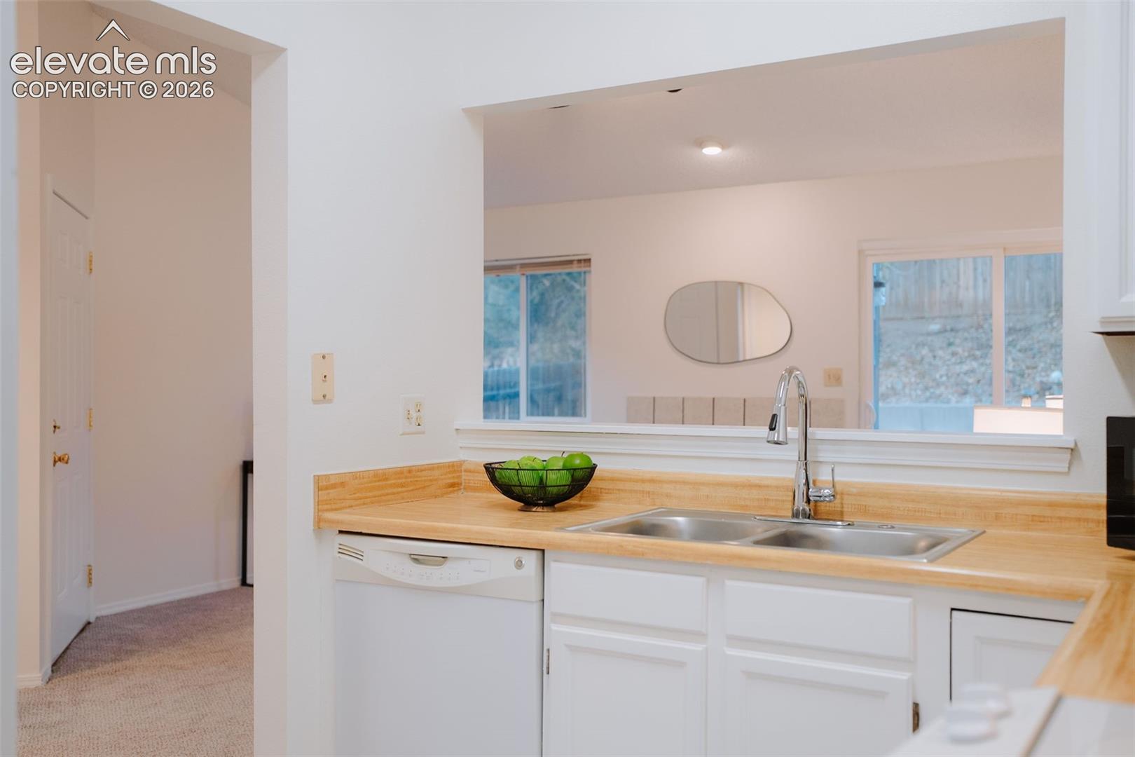 Kitchen featuring white cabinetry, light-toned laminate countertops, a stainless steel dual-basin sink with a pull-down faucet, and a built-in dishwasher