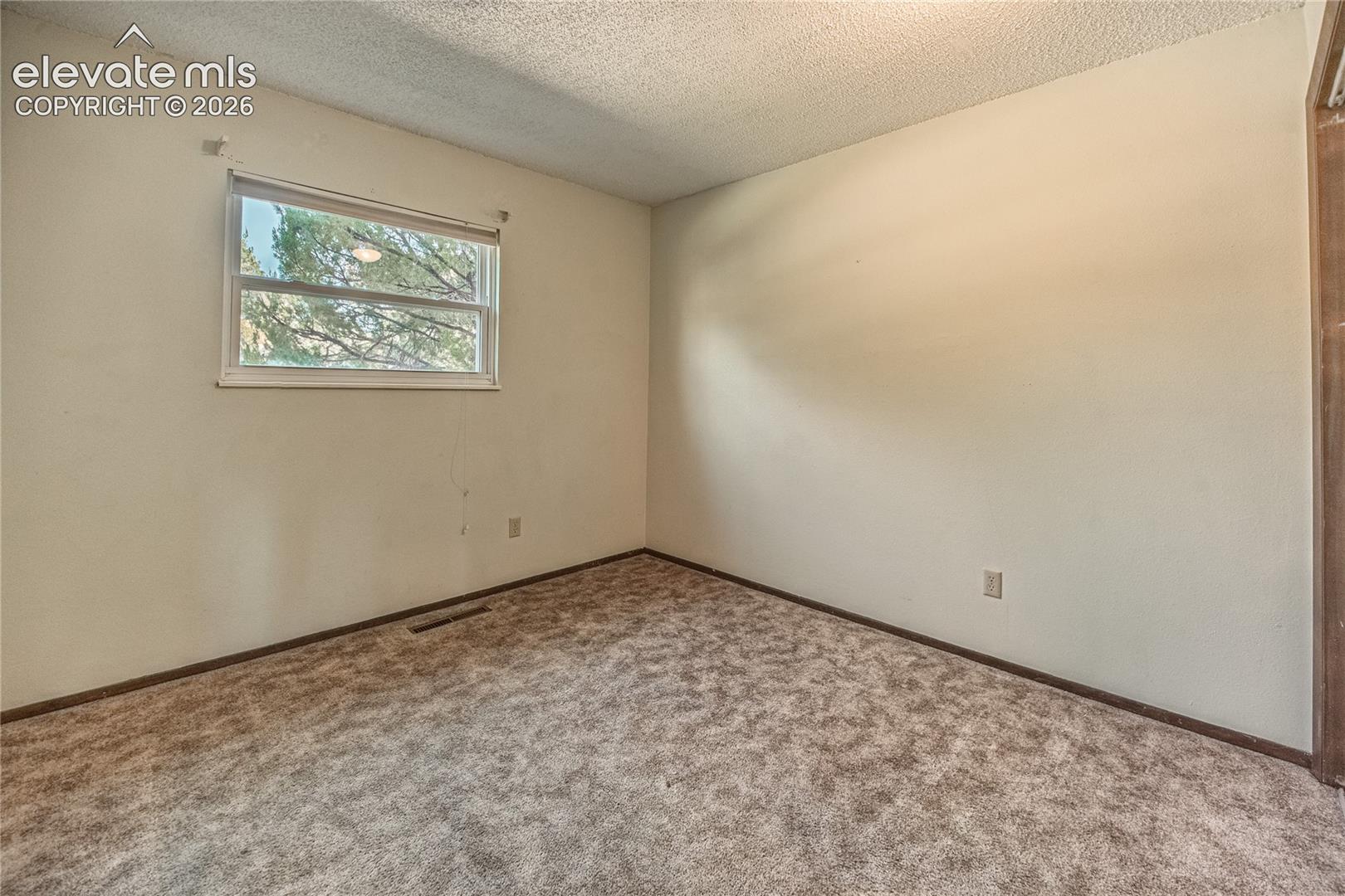 Interior room featuring textured ceiling, neutral wall finish, and wall-to-wall carpeting with a single window