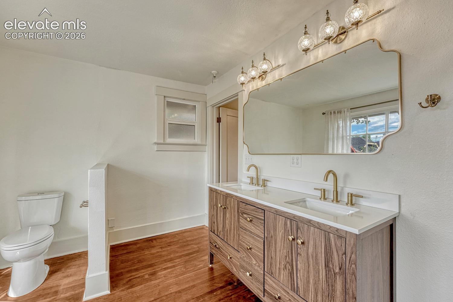 Dual vanity with wood-finish cabinetry, white countertop, and gold-toned fixtures