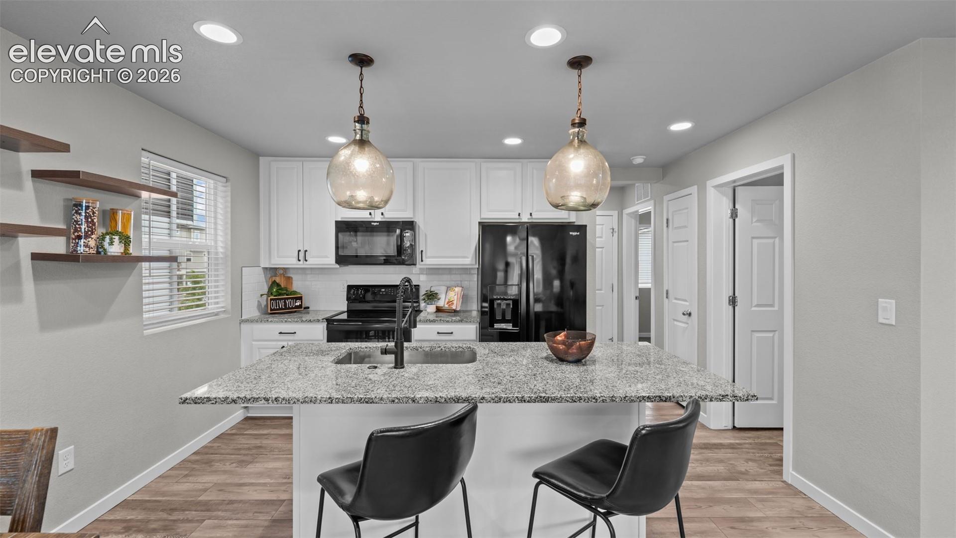 Kitchen featuring white shaker-style cabinetry, stone-finish countertops, center island with an undermount sink, recessed lighting, and wood-finish flooring