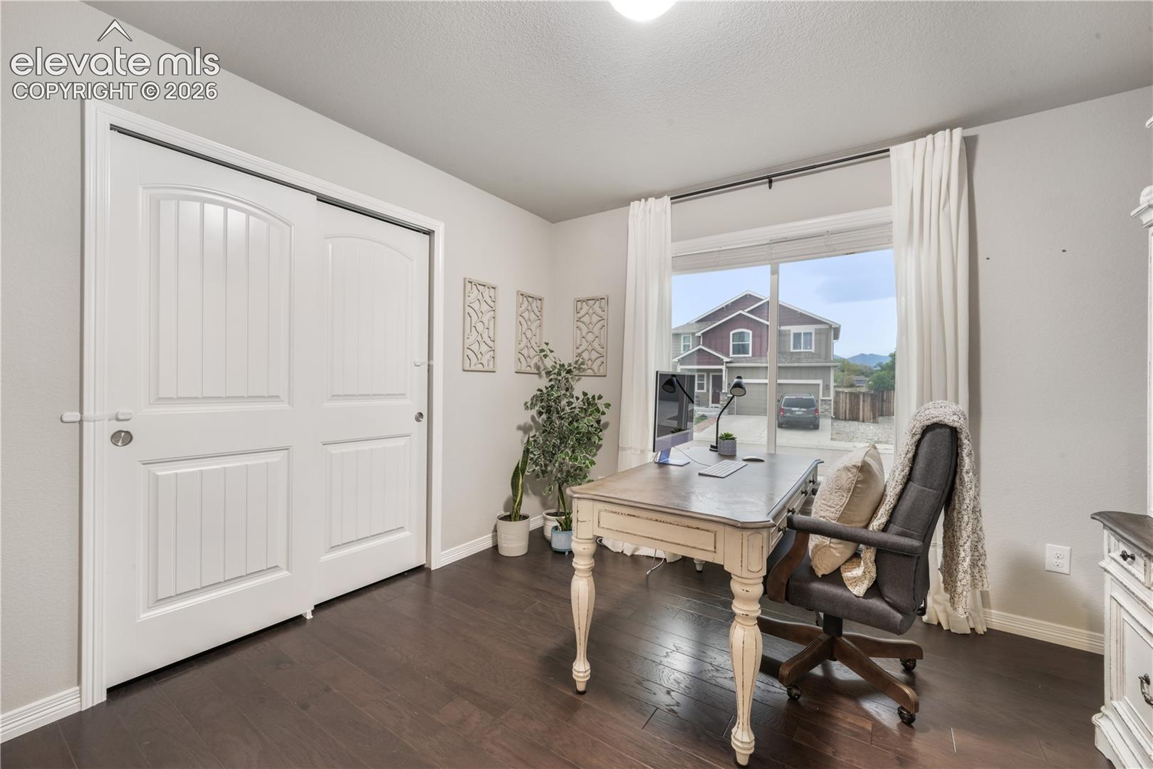 Room with dark wood-finish flooring, light-colored walls, and a large window with white curtains