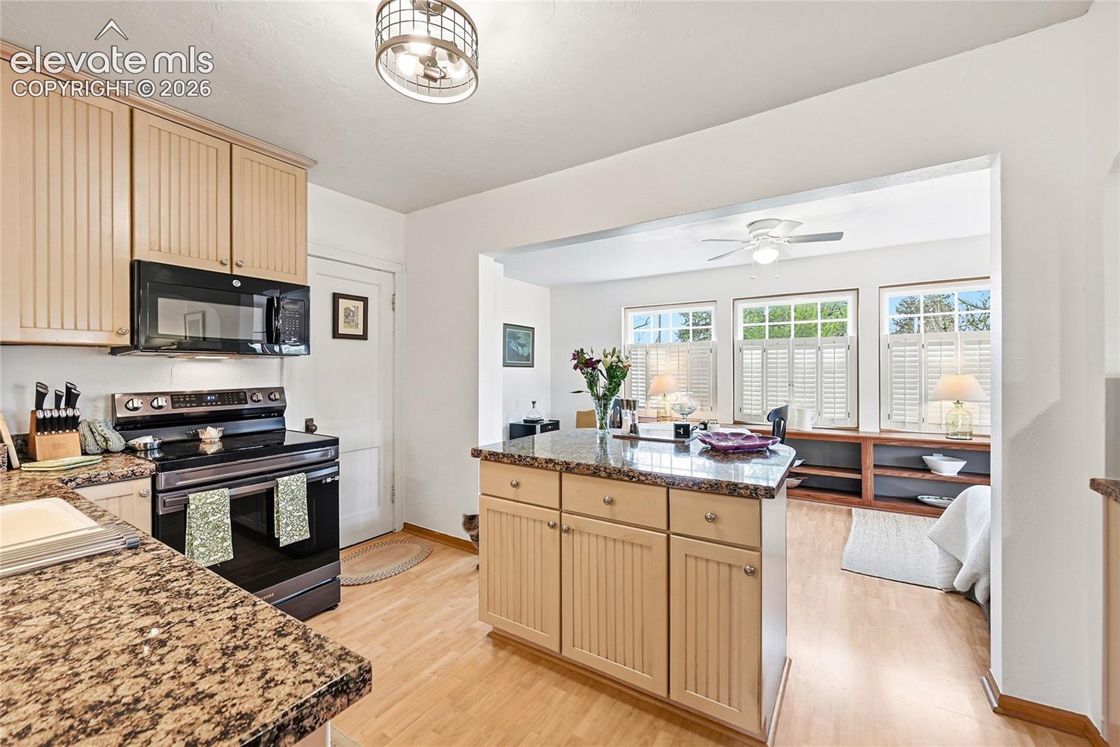 Kitchen featuring beadboard cabinetry, stone-surface countertops, built-in black appliances, wood-finish flooring, and a ceiling-mounted caged light fixture