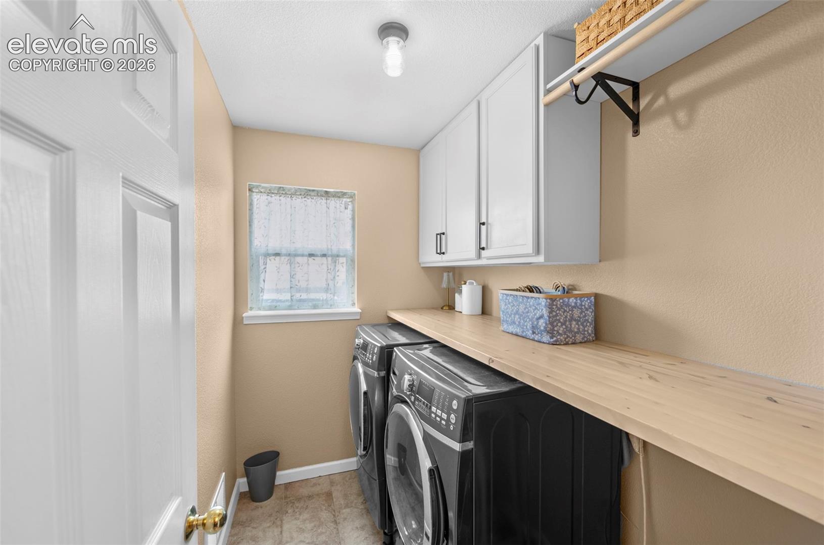 Dedicated laundry area featuring a wood-finish countertop, white cabinetry, and an upper shelf with a hanging rod